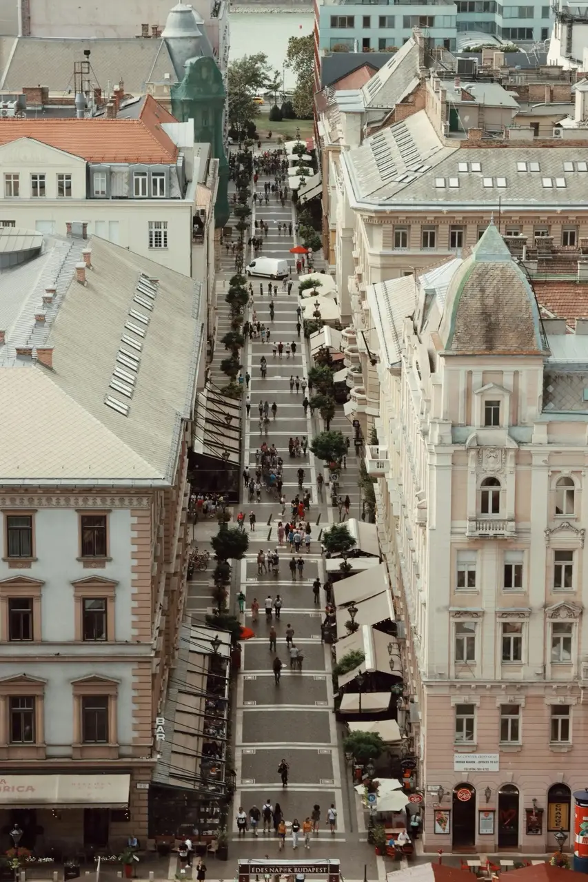 Aerial view of a busy pedestrian street lined with historic buildings and outdoor cafes in Budapest.
